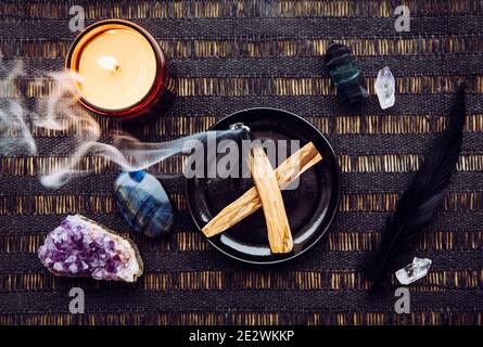 Flat lay view of Palo Santo wood known as oily aromatic holy wood sticks smouldering on plate on home table cleaning negative energy concept. Stock Photo