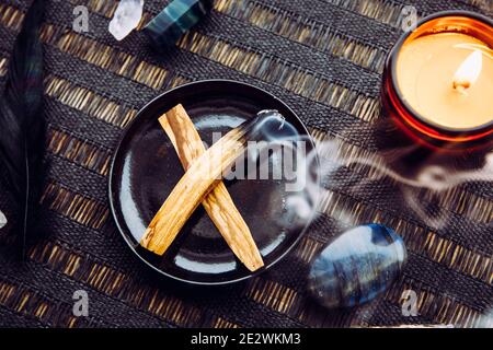 Flat lay view of Palo Santo wood known as oily aromatic holy wood sticks smouldering on plate on home table cleaning negative energy concept. Stock Photo