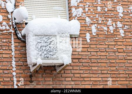 horizontal view in foreground of a brick facade with an air conditioning unit completely covered by snow below the window Stock Photo