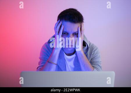 Gamer plays on a laptop. The programmer writes the code. Man on a colored background Stock Photo