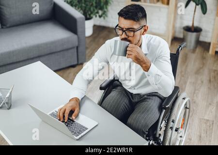 Disabled young businessman drinking coffee at his working table Stock Photo