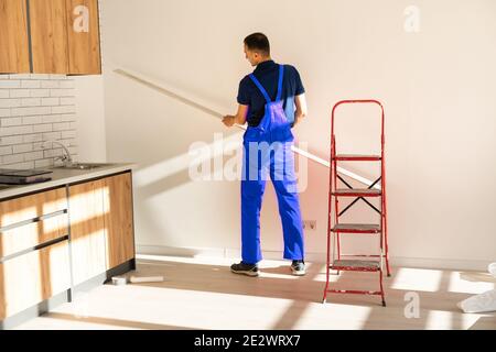 Rear back behind view photo of unrecognizable repairman master using rule to measure the required width of drywall and put label mark Stock Photo