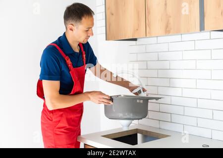 partial view of repairman in working overall fixing sink in kitchen Stock Photo