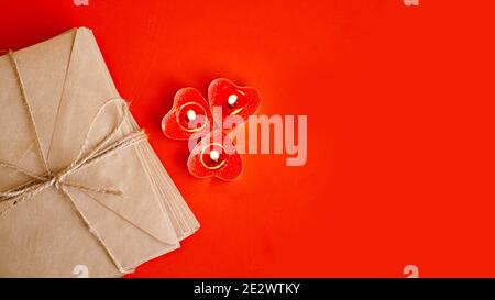 Kraft paper envelopes with red candles on a red background. Valentine day concept. Top view Stock Photo