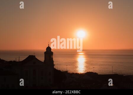 Early morning sunrise over water from Miradouro de Santa Luzia, Lisbon, Portugal. Silhouette of Alfama, Lisbon in the foreground. Stock Photo