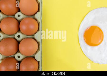 Raw brown eggs pack and a fried sunny side egg on yellow background Stock Photo