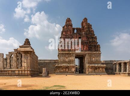 Hampi, Karnataka, India - November 5, 2013: Vijaya Vitthala Temple. Red Gopuram on yellow stone gate base seen from sandy coutyard under blue cloudsca Stock Photo