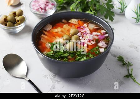 Greek tomato soup with vegetables, green olives and white beans in a dark bowl on a gray background. Closeup Stock Photo