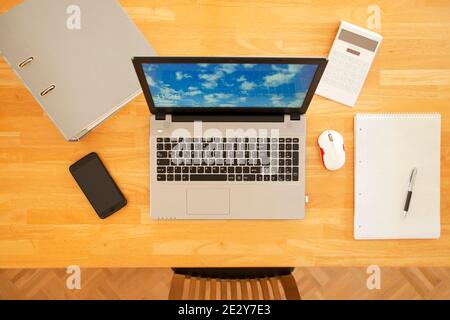 Overhead view of a workplace at home - wooden table with laptop, smart phone, calculator, file and mouse - overhead view - the photo an the sreen was Stock Photo