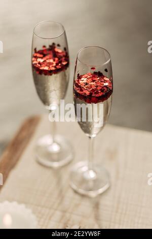 Happy Valentines day celebration concept. Close up of 2 two glasses with sparkling champagne and red heart shaped confetti. Love potion in glass Stock Photo