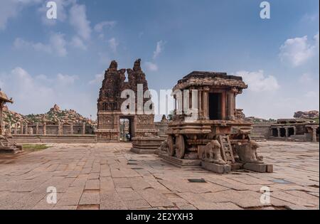Hampi, Karnataka, India - November 5, 2013: Vijaya Vitthala Temple. Wide view on brown stone chariot from the front under blue cloudscape with red sto Stock Photo
