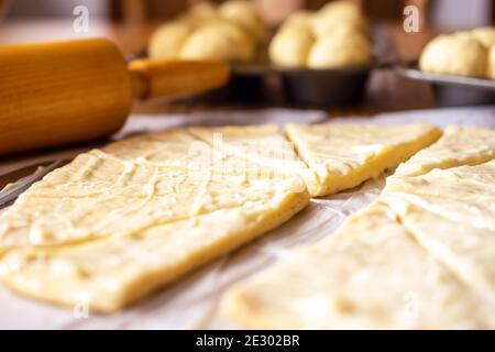 Rolling out raised yeast dough for crescent rolls.  Dough has been lathered in butter.  Wood rolling pin in background.  Dough on parchment paper.  Ad Stock Photo
