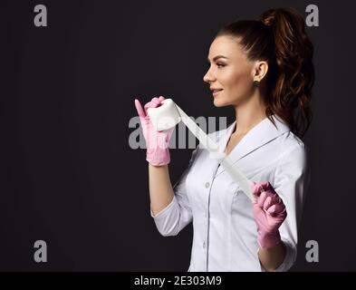 Profile of pretty woman doctor gynecologist or nurse in pink latex gloves and uniform stands holding medical bandage Stock Photo