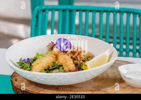 Buttered fish and green salad with sauce and lemon, decorated with butterfly pea flowers. Served on a white ceramic plate. Stock Photo