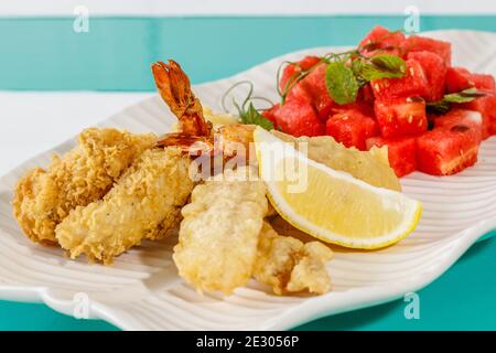 Battered prawns, salad with fresh watermelon and mint, and lemon. Served on a white ceramic plate. Stock Photo
