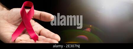 Red awareness ribbon in the hands of a man on a dark background with a place for text for the concept of World AIDS Day. Stock Photo