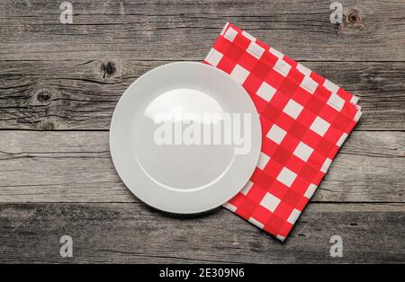 White porcelain plate and red checkered napkin on an old wooden table. Top view Stock Photo
