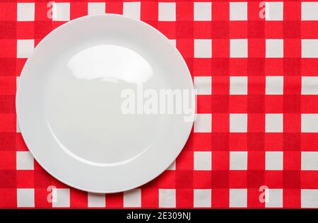 White porcelain plate on a red checkered tablecloth. View from above Stock Photo