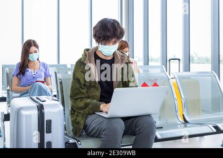 Traveler wearing protective mask in airport, during Covid-19 pandemic, with social distancing protocol. Using laptop computer while waiting for flight Stock Photo