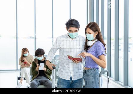 Couple travelers wearing protective mask in airport, during Covid-19 pandemic, with social distancing protocol. Holding and pointing at passport and d Stock Photo