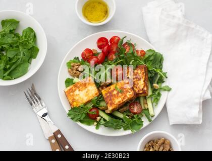 Fresh salad from arugula, cherry tomatoes, cucumbers and roasted cheese on a gray stone background. top view. delicious healthy food Stock Photo