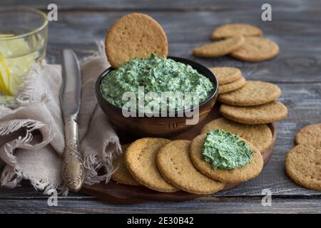 Green spinach dip with cream cheese, garlic and spices on a wooden board with oat crackers, rustic style, selective focus. Healthy homemade food Stock Photo