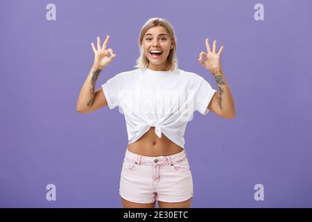 Girl being agree with friends deciding were enjoy holidays. Portrait of charming satisfied and happy young blonde female with tattoos and pierced Stock Photo
