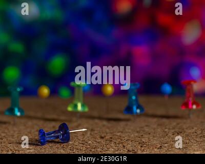 A group of colorful thumbtacks are on a cork surface against a very colorful background Stock Photo