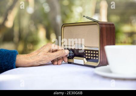 Senior woman hand turning knob on vintage radio in backyard. Stock Photo