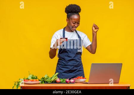 african chef feeling happy and excited while using her laptop and holding her credit card Stock Photo