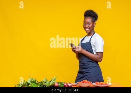 female african chef smiling while holding her phone and looking forward at the camera Stock Photo