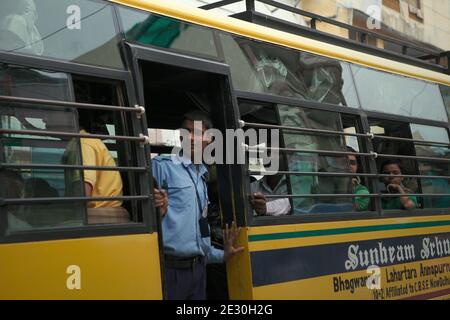 A student looking out of the entrance door of a school bus moving on a busy street in Varanasi, Uttar Pradesh, India. Stock Photo