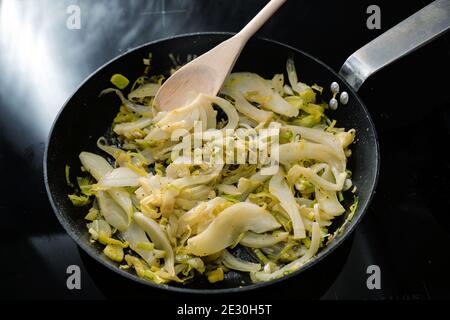 Fennel slices and leek in a black frying pan on the stove, cooking vegetarian with healthy vegetables, selected focus, narrow depth of field Stock Photo