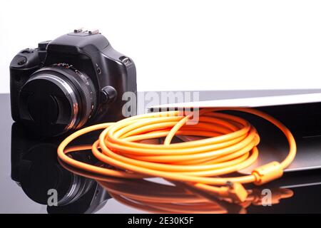 Digital photo camera connected to laptop with orange rolled cable. Stock Photo