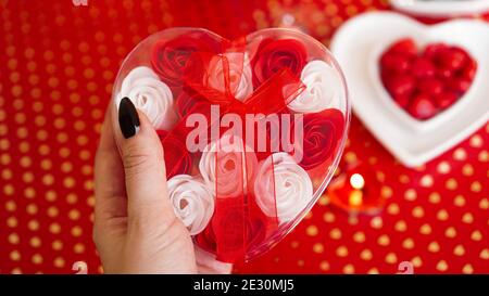Woman hands holding a gift box in heart shape with beautiful roses over red festive background. Concept of giving a gift on Valentines day holidays Stock Photo