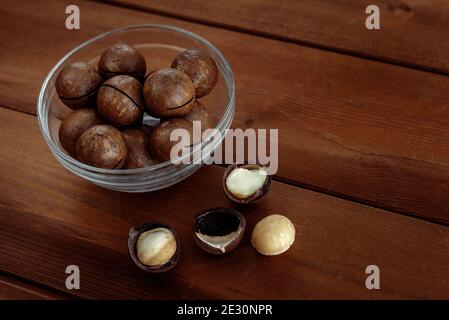 Macadamia with kernel nuts and nutshell in bowl on wooden table. Healthy food and snack Stock Photo