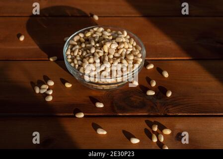 Pine nuts in bowl under natural sunlight on wooden table. Healthy food and snack Stock Photo