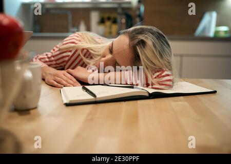 A female student fell asleep while studying in a relaxed atmosphere at the kitchen. Student, tired, studying Stock Photo