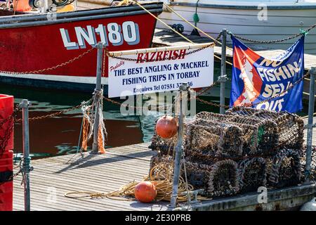 Torquay Inner Harbour Walkway Detail with Lobster Pots and Moored Fishing Boats With Political Banner ‘No Fishing Sell Out’.  A Popular Visitor Stop. Stock Photo