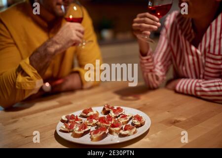 A young couple enjoying food and wine in a relaxed atmosphere at the kitchen. Dinner, relationship, together, home Stock Photo