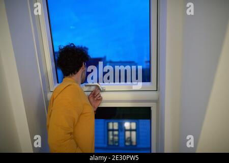 A young guy looking through the window in the home on a beautiful early morning. Morning, home, routine Stock Photo