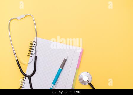 medical stethoscope with pen and notebook on yellow background with a copy space Stock Photo