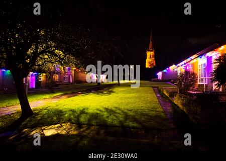 Christmas decorations in a Bedfordshire village - coloured lights on bungalows with the illuminated tower of the parish church in the distance Stock Photo
