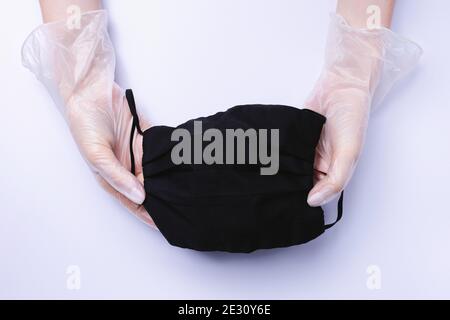 Female hands in gloves stretch a black medical mask on a white background. Stock Photo
