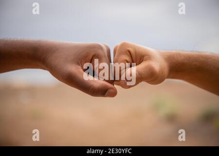Hands of different color to fight racism. Two fists touch, one is white (caucasian) the other is black (african) Stock Photo