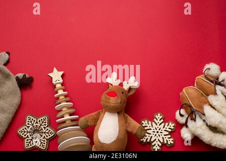 baby christmas background, child winter flat lay wood decor tree and snowflakes, deer, cloth hat, boots on red background, copy space Stock Photo