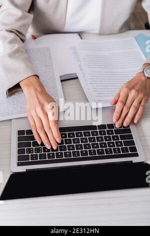 partial view of translator typing on laptop near documents in office Stock Photo