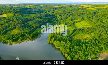 Aerial view over lake next to the colorful forest on hilly landscape, treetops Stock Photo