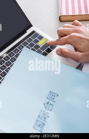 cropped view of interpreter pressing translation key on laptop near paper with chinese hieroglyphs on blurred foreground Stock Photo