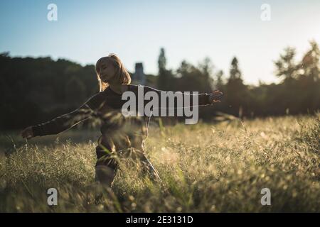 A young woman dancing in tall grass during golden hour Stock Photo
